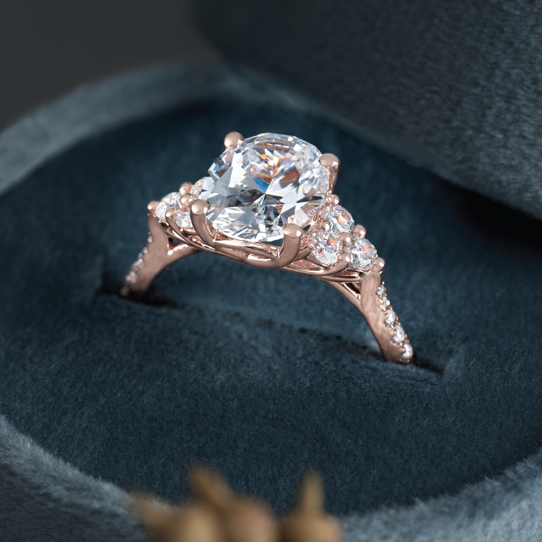 Closeup of a ring that at first appears to be a three-stone design in 14k rose gold with accent stones. Upon closer inspection, it actually has 3 stones on each side, making this a seven-stone design!