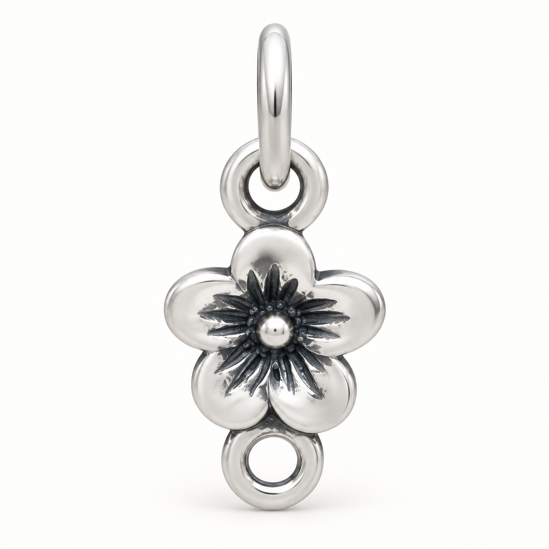 A polished silver flower charm pendant with a five-petal design, featuring an oxidized dark center and a hanging loop at the top, shown on a clean white background.