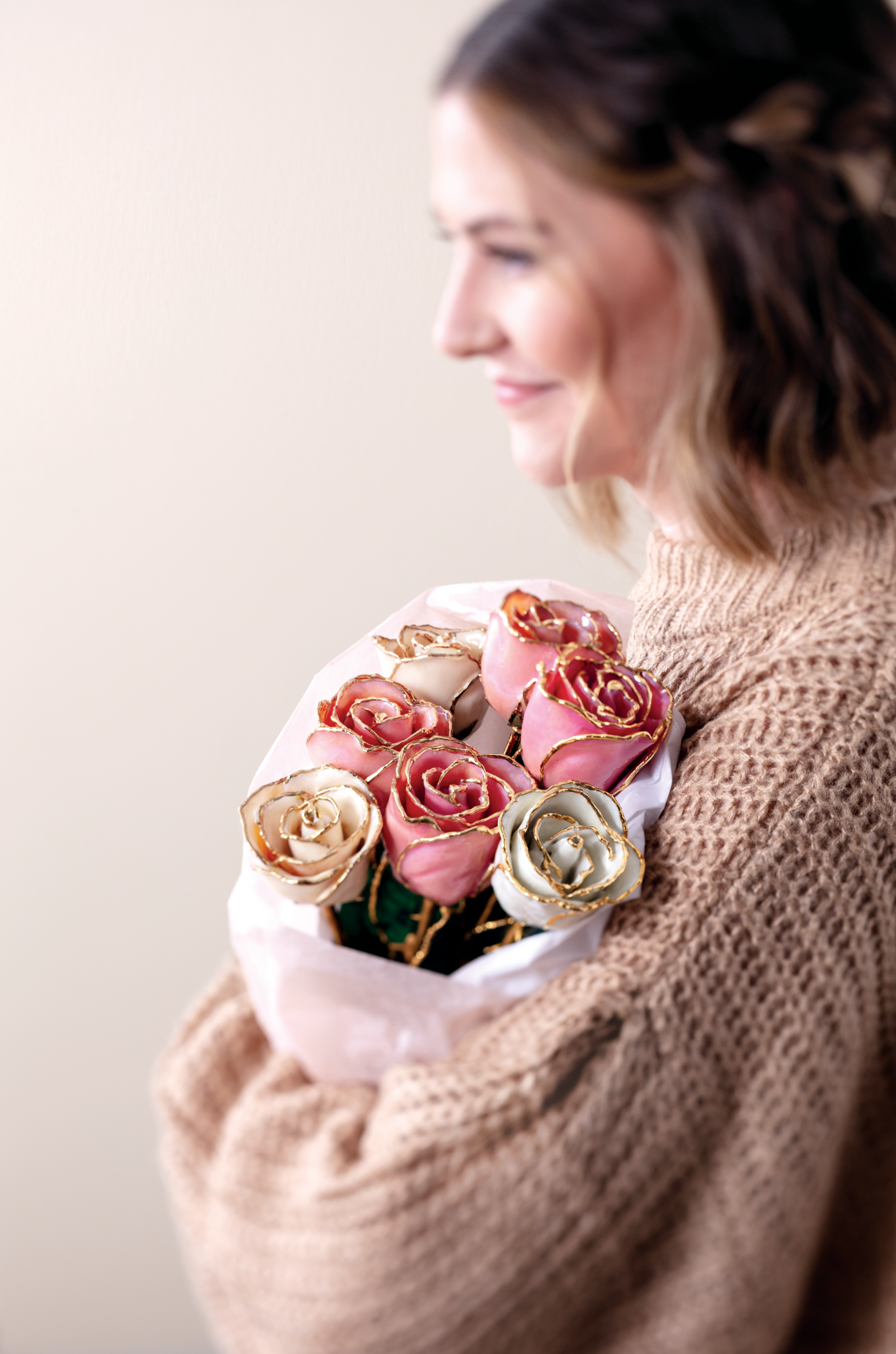 A smiling woman holding a bouquet of pink and white Everlasting Roses, hand painted with 24k gold trim.