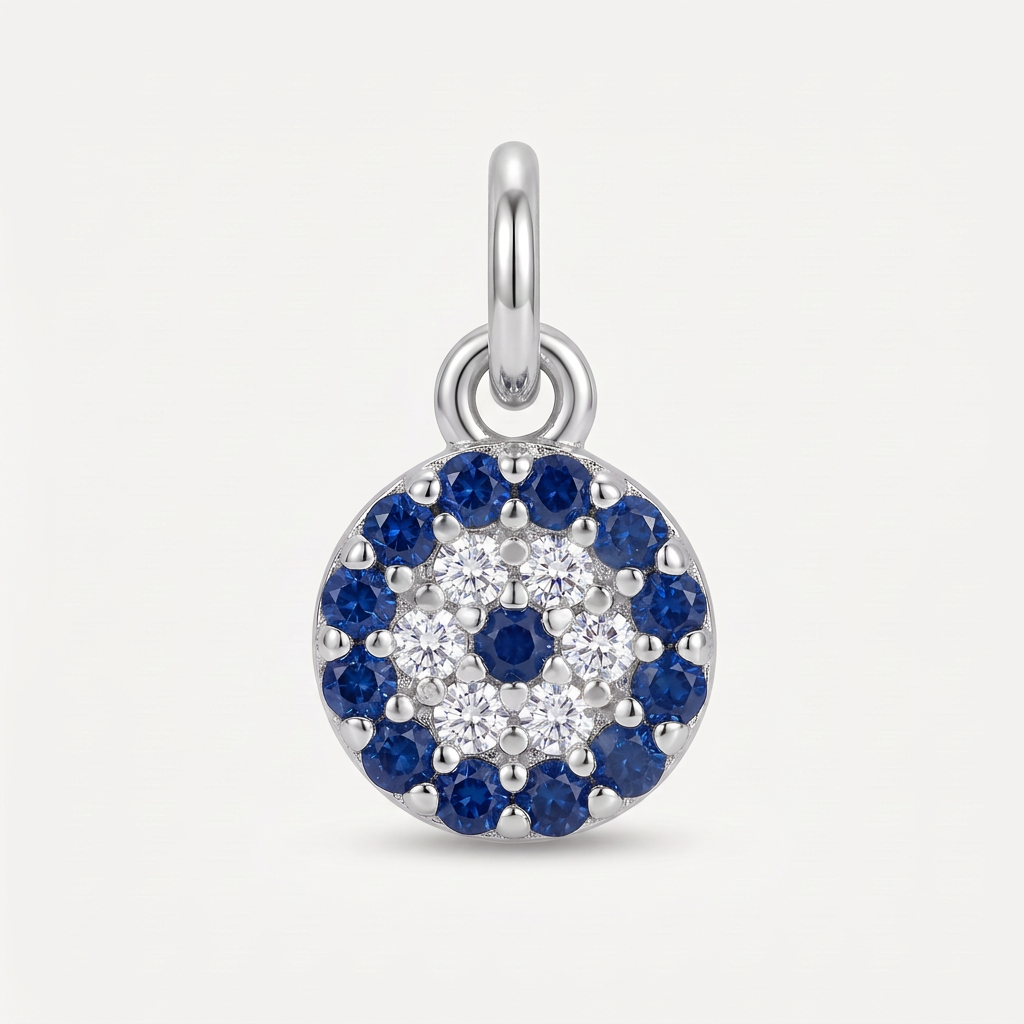 A round sterling silver charm pendant featuring a multi-layered evil eye design with blue sapphires and clear cubic zirconia stones, shown on a light gray background.