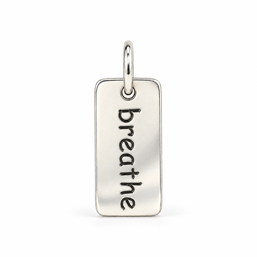 Rectangular sterling silver tag charm with rounded corners, engraved with “breathe” in lowercase letters, with a silver jump ring.