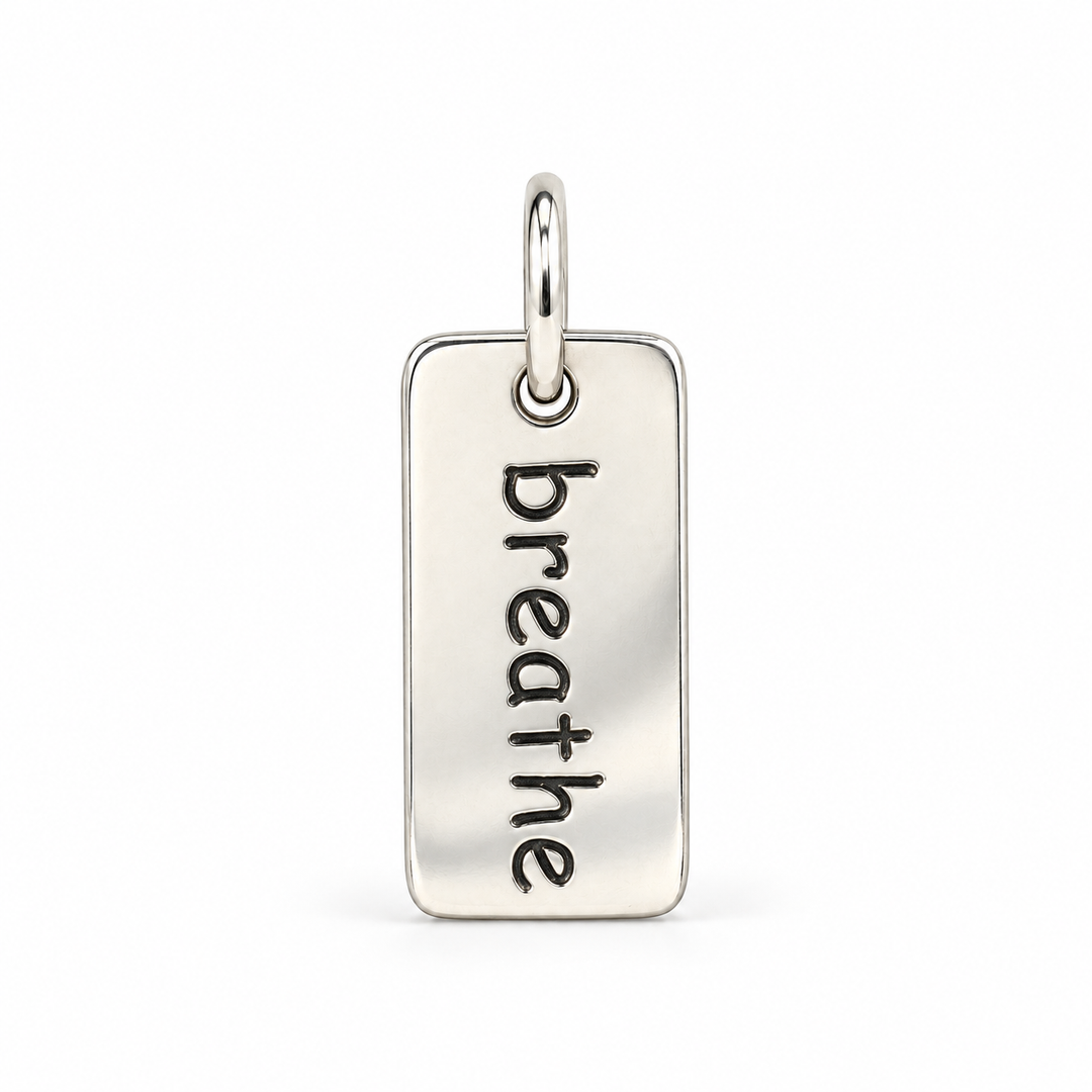 Rectangular sterling silver tag charm with rounded corners, engraved with “breathe” in lowercase letters, with a silver jump ring.