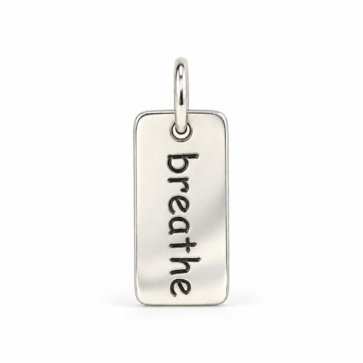 Rectangular sterling silver tag charm with rounded corners, engraved with “breathe” in lowercase letters, with a silver jump ring.