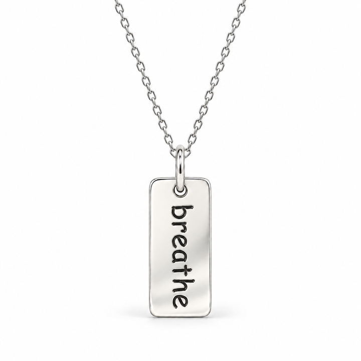 Sterling silver necklace with a rectangular tag pendant engraved with “breathe” in lowercase letters, suspended from a fine cable chain.