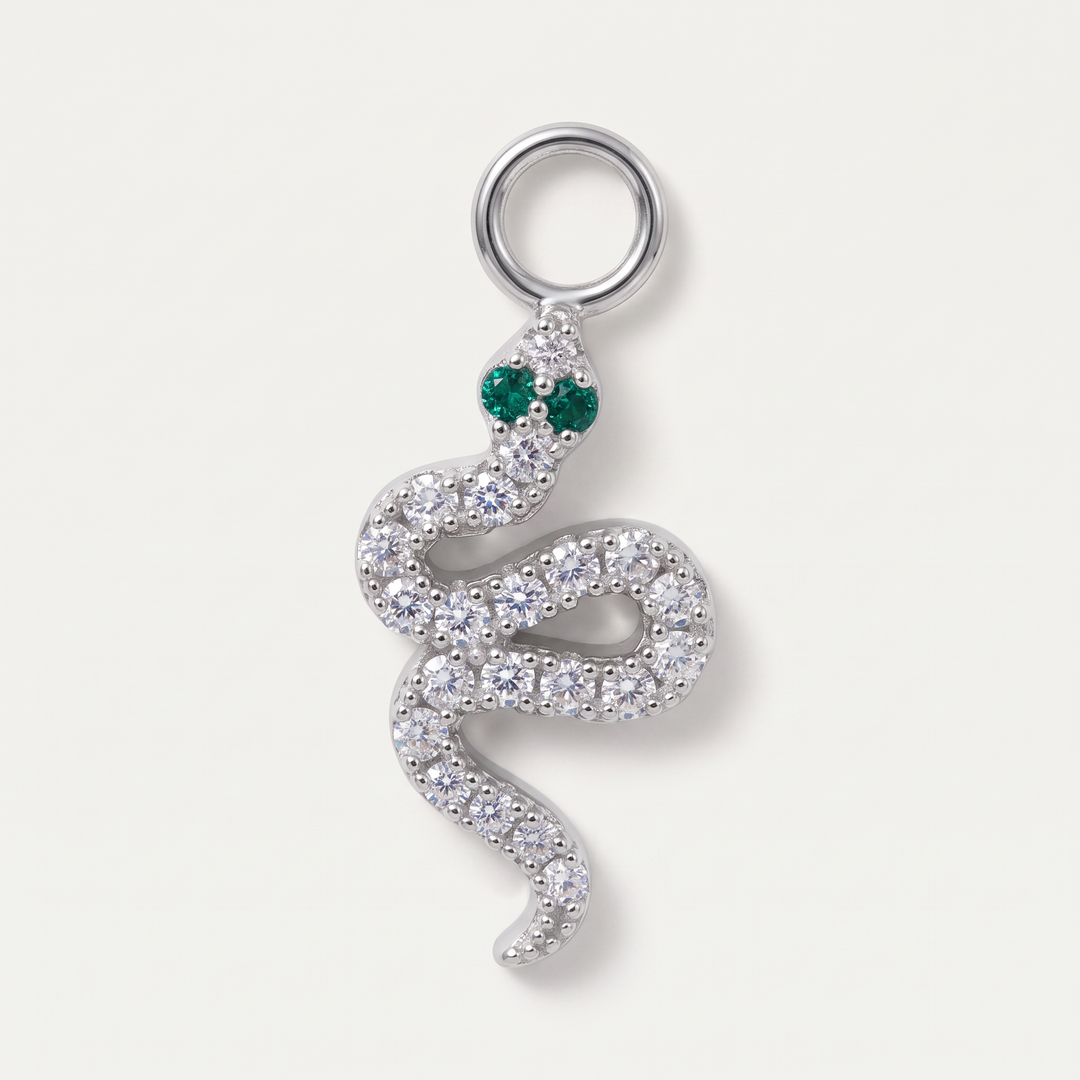A silver snake pendant adorned with clear pavé stones and featuring green gemstone eyes, set against a light off-white background.