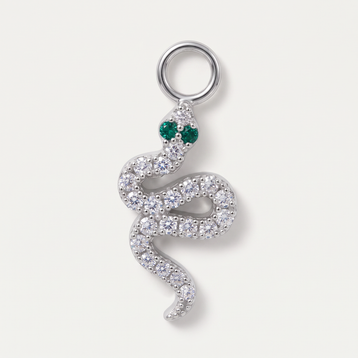 A silver snake pendant adorned with clear pavé stones and featuring green gemstone eyes, set against a light off-white background.