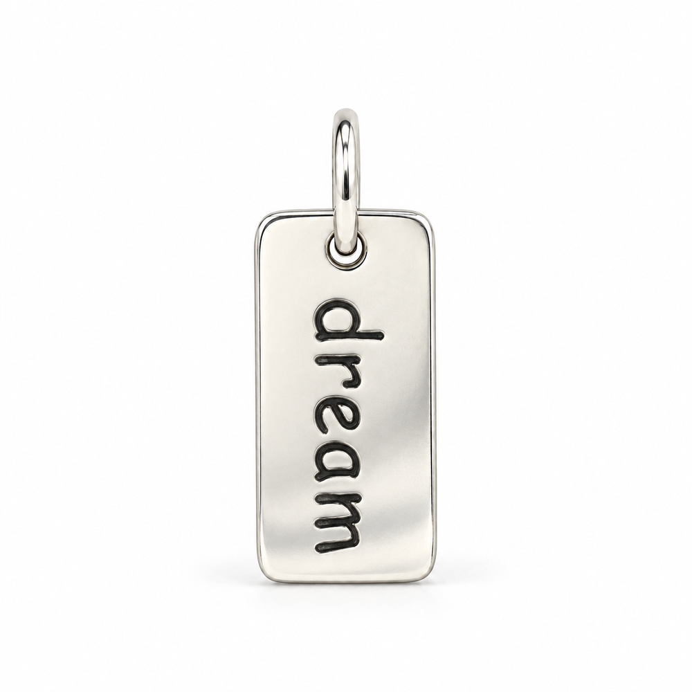 Rectangular sterling silver tag charm with rounded corners, engraved with “dream” in lowercase letters, with a silver jump ring.