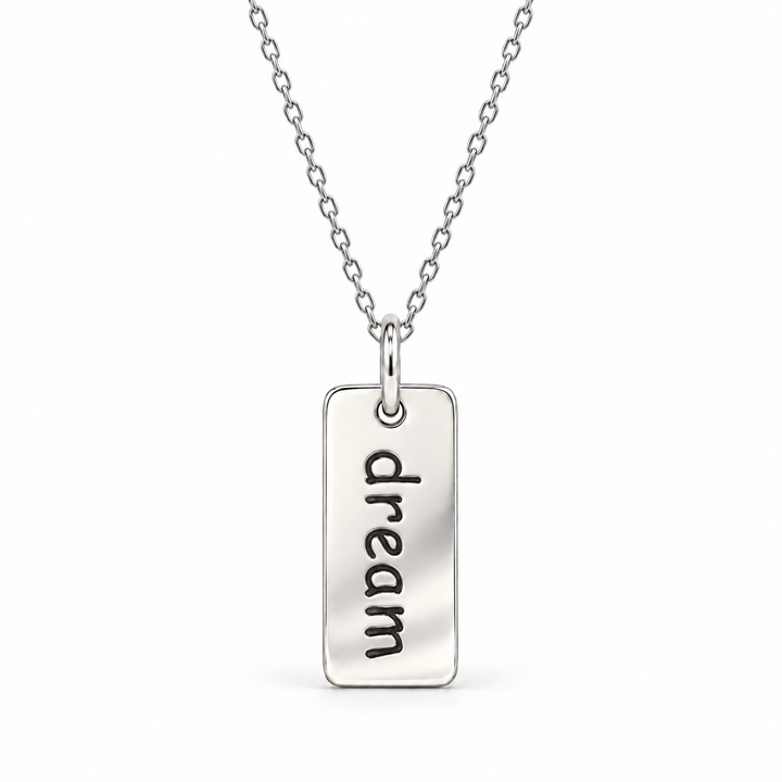 Sterling silver necklace with a rectangular tag pendant engraved with “dream” in lowercase letters, suspended from a fine cable chain.