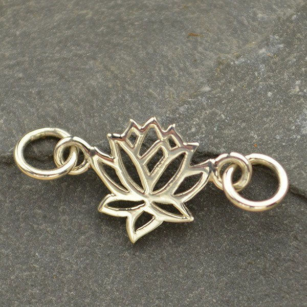 Sterling silver openwork lotus connector charm with attachment rings on both sides, front angled view on slate.