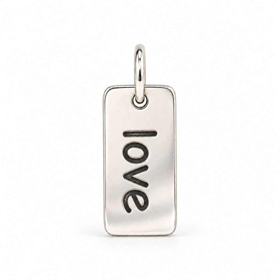 Rectangular sterling silver tag charm with rounded corners, engraved with “love” in lowercase letters, with a silver jump ring.