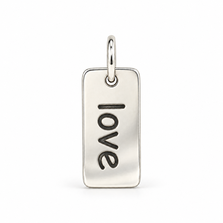 Rectangular sterling silver tag charm with rounded corners, engraved with “love” in lowercase letters, with a silver jump ring.