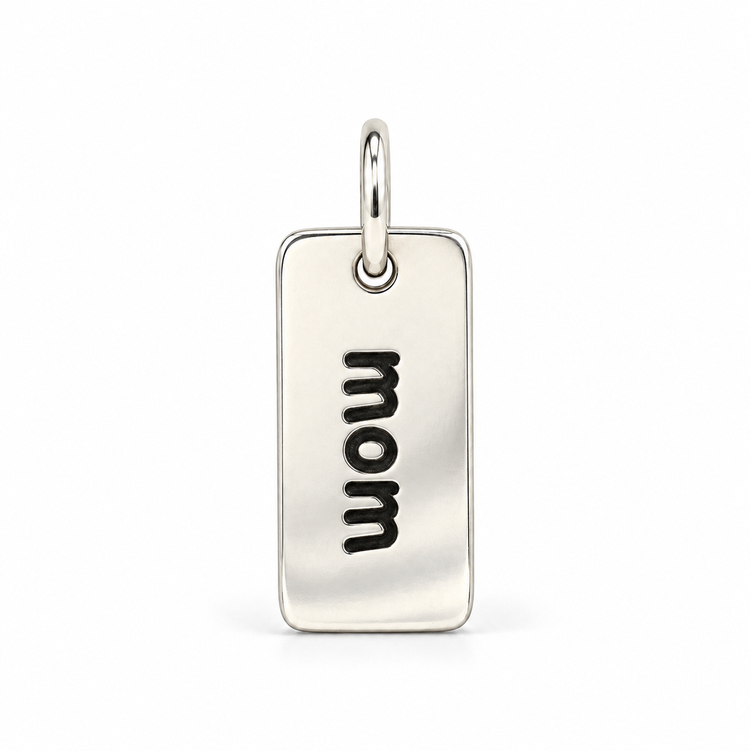 Rectangular sterling silver tag charm with rounded corners, engraved with “mom” in lowercase letters, with a silver jump ring.