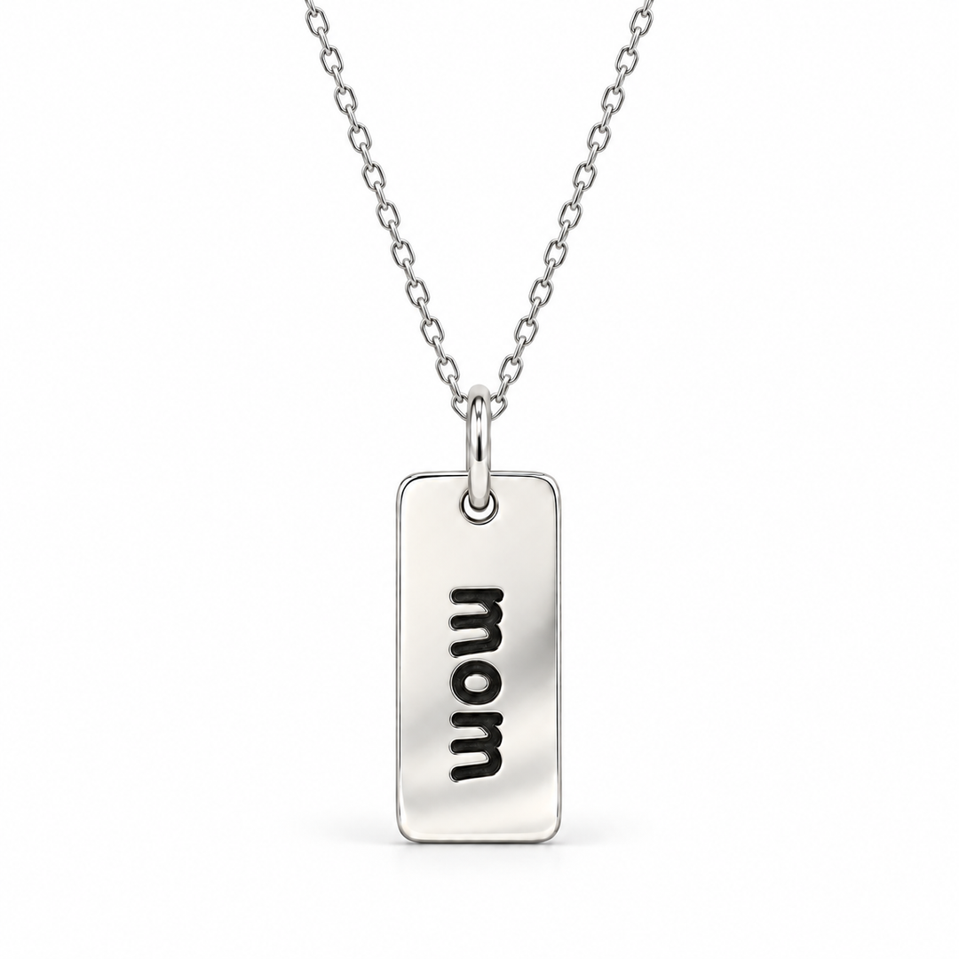 Sterling silver necklace with a rectangular tag pendant engraved with “mom” in lowercase letters, suspended from a fine cable chain.
