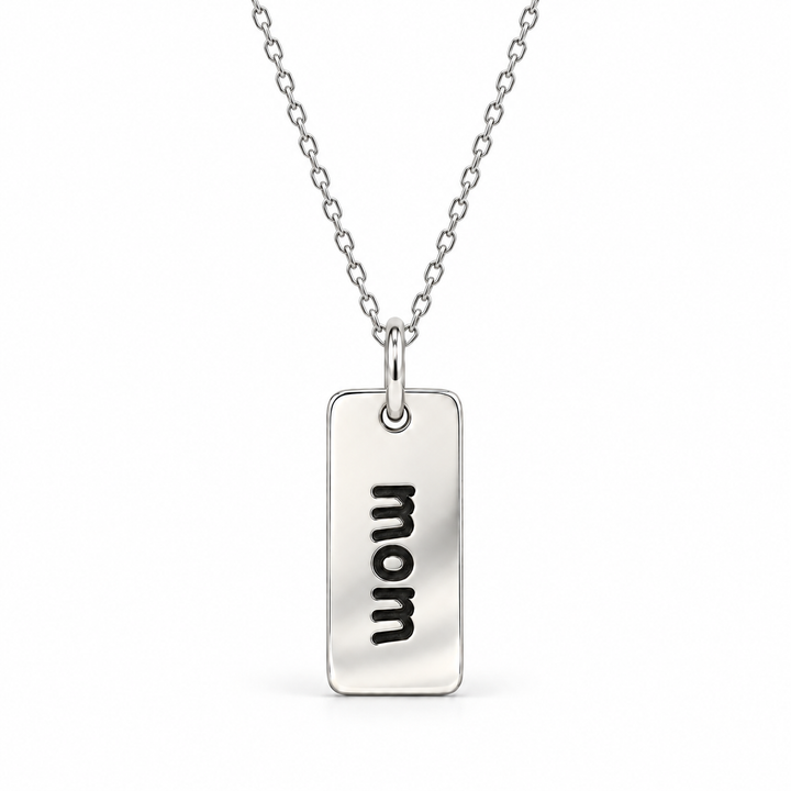 Sterling silver necklace with a rectangular tag pendant engraved with “mom” in lowercase letters, suspended from a fine cable chain.