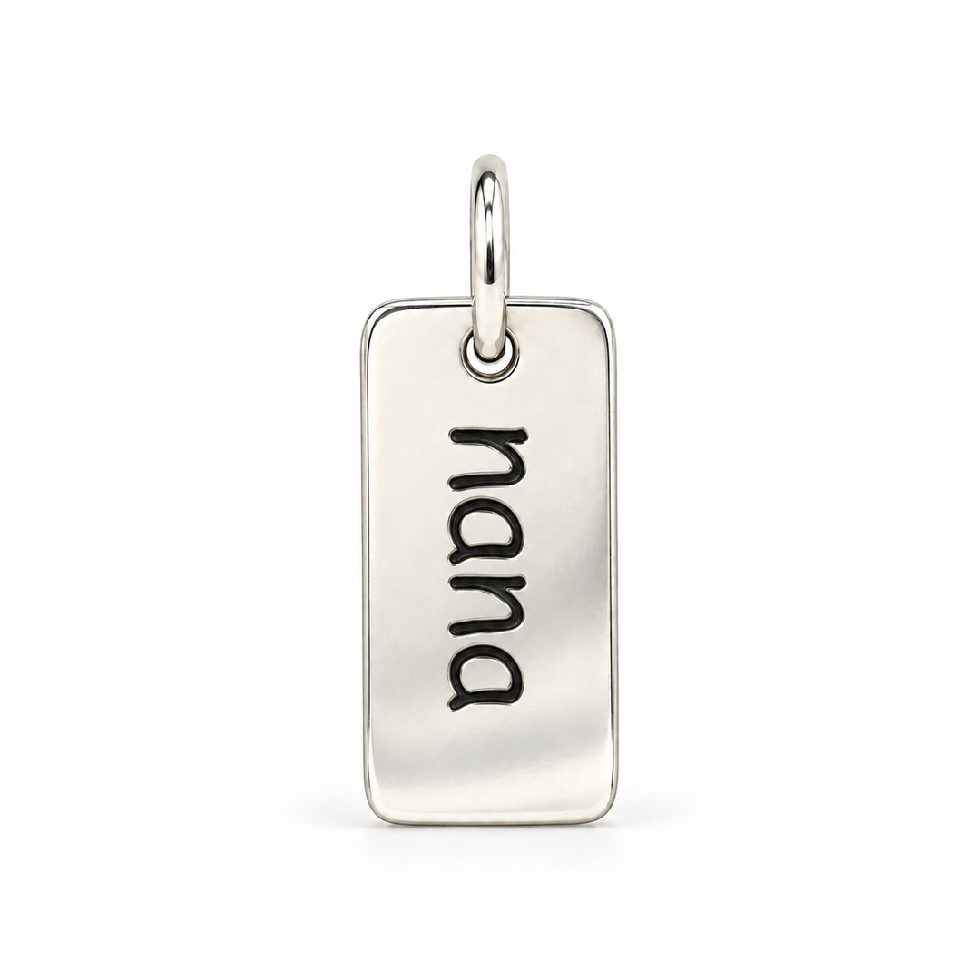 Rectangular sterling silver tag charm with rounded corners, engraved with “nana” in lowercase letters, with a silver jump ring.