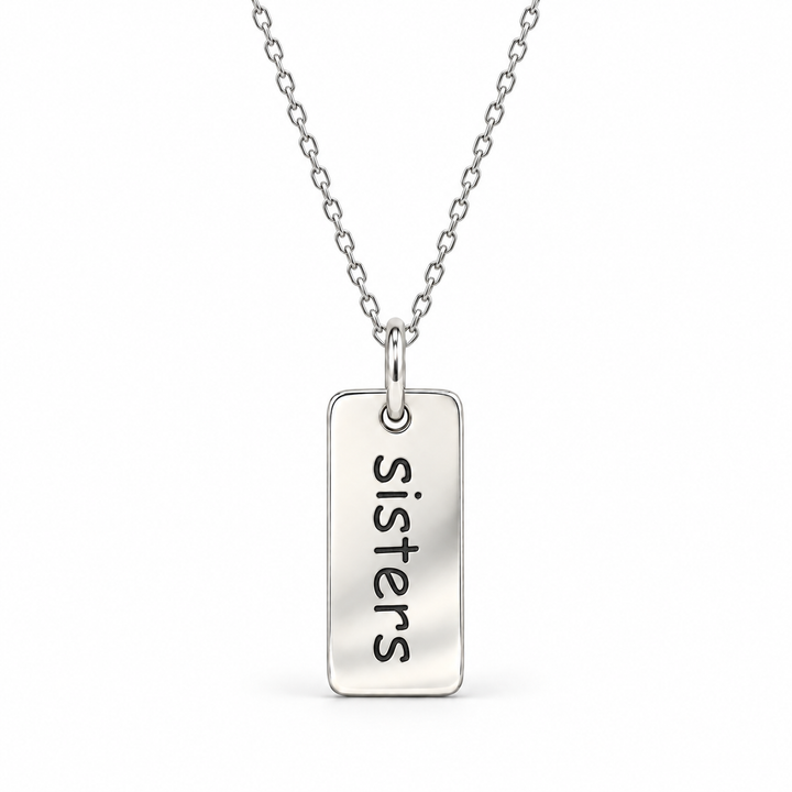 Sterling silver necklace with a rectangular tag pendant engraved with “sisters” in lowercase letters, suspended from a fine cable chain.